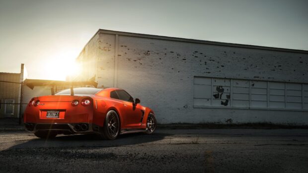 A red Nissan Gt R is parked with sunlight shining near an old brick wall, HD Desktop Wallpaper