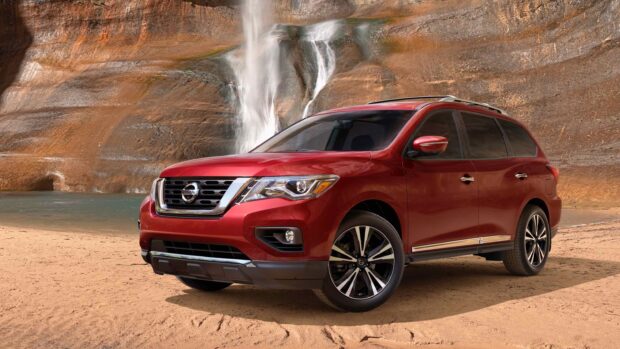 A red Nissan Pathfinder stands on sandy ground near a rocky waterfall, 2K Desktop Wallpaper