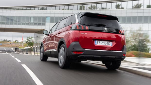 A Peugeot 5008 drives on an urban road with a modern building in the background, 4K Desktop Wallpaper