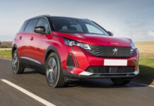 A red Peugeot 5008 drives on a clear road with fields in the background, 2K Desktop Wallpaper