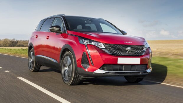 A red Peugeot 5008 drives on a clear road with fields in the background, 2K Desktop Wallpaper