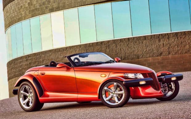 A red Plymouth Prowler convertible is parked near a modern curved building, 2K Desktop Wallpaper