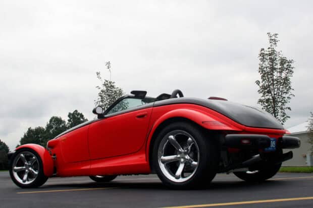 A red Plymouth Prowler convertible is parked on an asphalt road with trees and a cloudy sky in the background, 2K Desktop Wallpaper