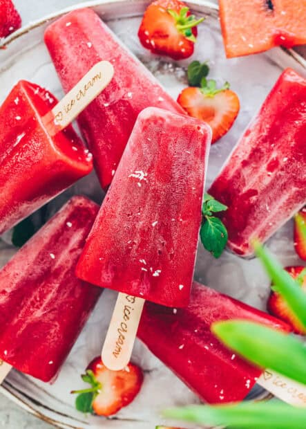 A red popsicle lays on a plate surrounded by fresh strawberries and mint leaves, HD Mobile Wallpaper