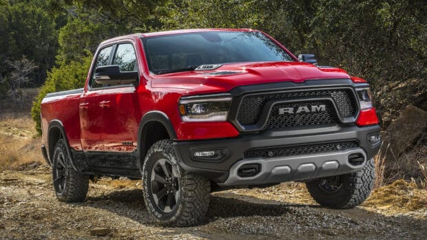 A red Ram pickup is parked on rocky terrain surrounded by trees and shrubs, HD Desktop Wallpaper