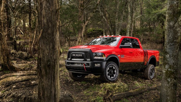 A red Ram truck is parked on rugged terrain surrounded by trees and rocks in a forest, 4K Desktop Wallpaper