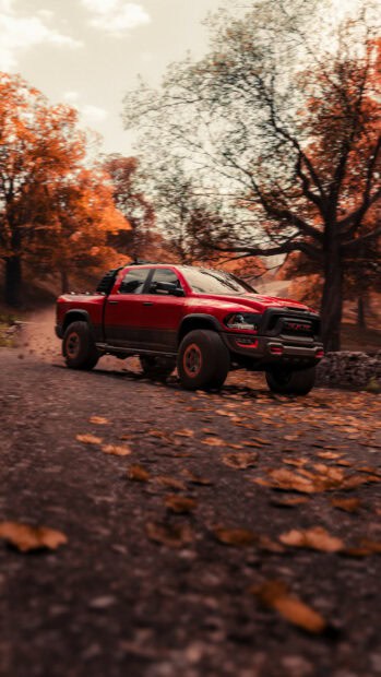 A red Ram truck is driving fast on a road covered with autumn leaves, surrounded by fall trees, 2K Mobile Wallpaper