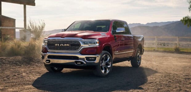 A red Ram truck is parked on a dirt road beside a wooden fence with mountains in the background, 2K Desktop Wallpaper
