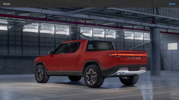 A red Rivian pickup truck is parked inside a spacious industrial building with bright windows, HD Desktop Wallpaper