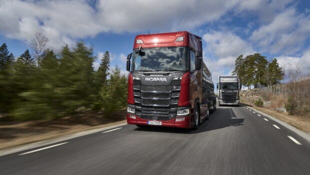 A red Scania truck and a black Scania truck are driving on a scenic road with trees and a cloudy sky, 4K Desktop Wallpaper