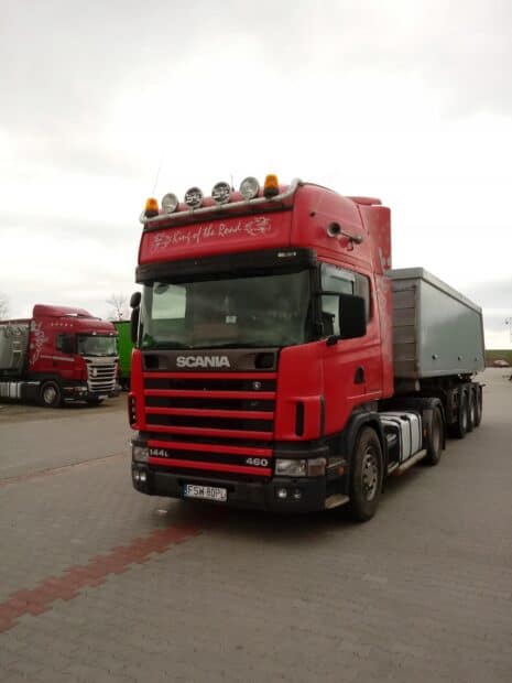 A red Scania truck with a trailer is parked on a paved lot under a cloudy sky, 2K Desktop Wallpaper