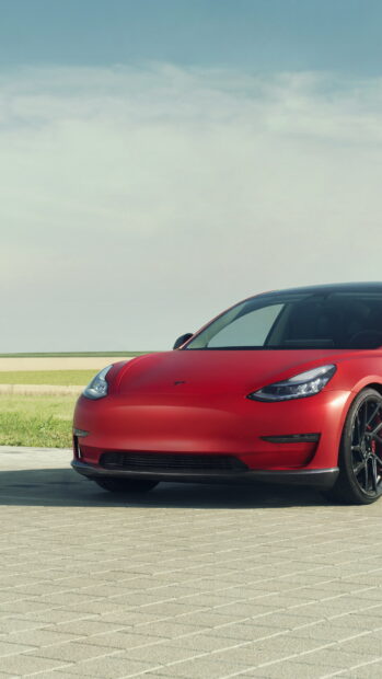 A red Tesla Model 3 is parked on a paved area in front of a clear sky with open fields, 4K Phone Wallpaper