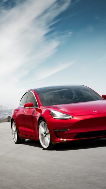 A red Tesla Model 3 driving under a blue sky with clouds, 2K Phone Wallpaper