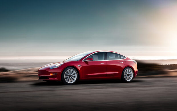A red Tesla Model 3 drives swiftly along a blurred desert road at sunset, HD Desktop Wallpaper
