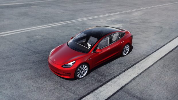 A red Tesla Model 3 is parked on the asphalt near white road markings, 4K Desktop Wallpaper