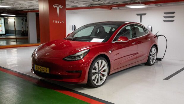 A red Tesla Model 3 is plugged in and charging in a parking lot, HD Desktop Wallpaper