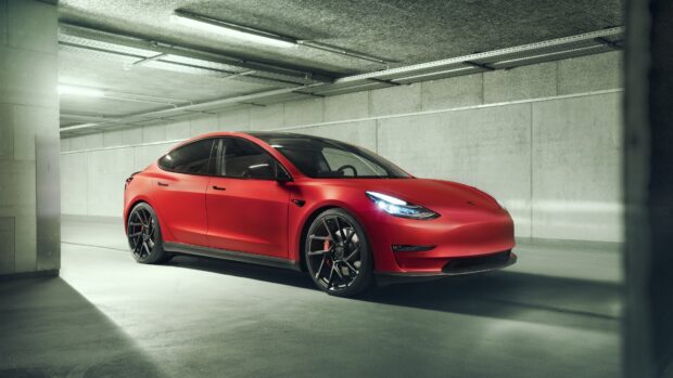 A red Tesla Model 3 is parked inside a modern concrete garage with soft lighting, 4K Desktop Wallpaper