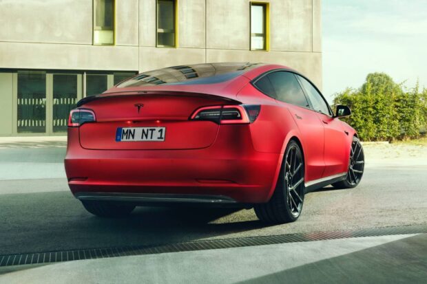 A red Tesla Model 3 is parked outdoors beside a modern building with greenery in the background, HD Desktop Wallpaper