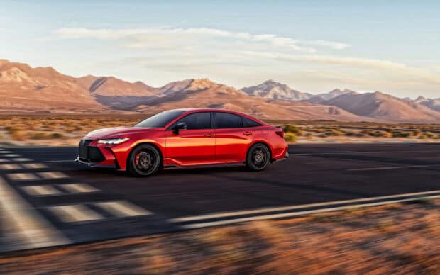 A red Toyota Avalon is driving fast on a desert highway with mountains in the background, 2K Desktop Wallpaper