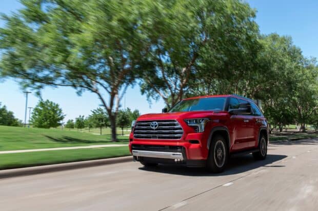 A red Toyota Sequoia drives past green trees on a clear day, HD Desktop Wallpaper