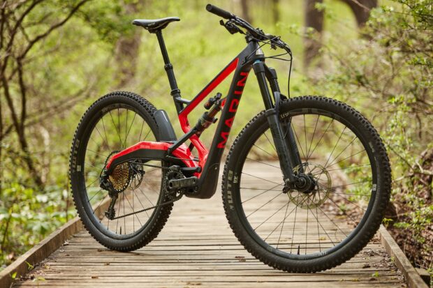 A red and black Marin bike standing on a wooden trail surrounded by green forest, 2K Desktop Wallpaper