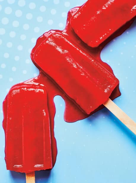A red popsicle melting on a dotted blue surface with visible liquid pooling around it, 2K Mobile Wallpaper