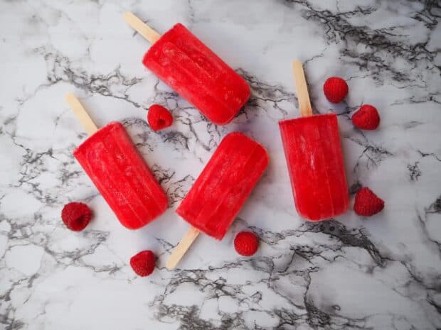 Red popsicles are arranged with fresh raspberries on a marble surface, 2K Desktop Wallpaper