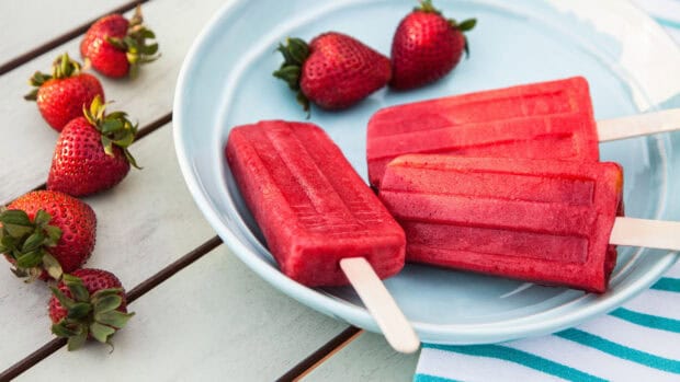 A plate with three red popsicles and fresh strawberries arranged next to them on a wooden table, 4K Desktop Wallpaper