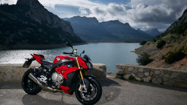 A red street bike is parked by a stone wall with mountains and a calm lake in the background, 4K Desktop Wallpaper