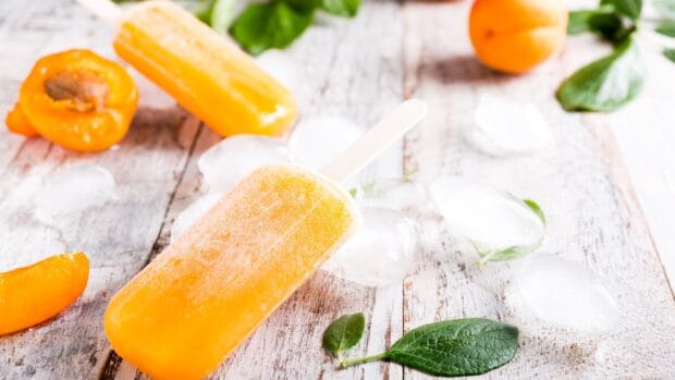 A refreshing apricot popsicle with ice cubes and fresh apricots on a rustic wooden surface, 4K Desktop Wallpaper
