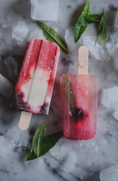 Two colorful popsicles resting on ice with green leaves, 2K Mobile Wallpaper