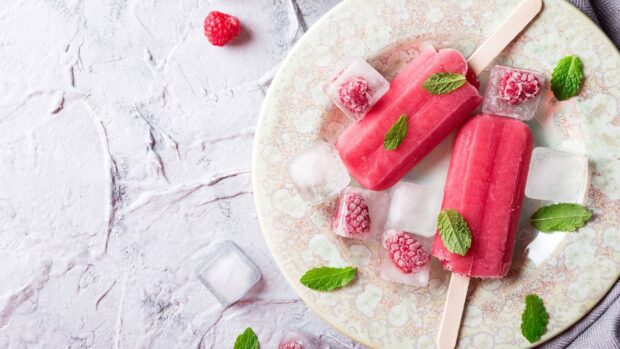 A red popsicle surrounded by ice cubes, raspberries, and mint leaves on a decorated plate, HD Desktop Wallpaper