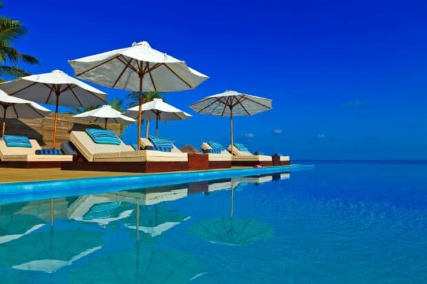 White beach umbrellas with lounge chairs are reflected in the clear pool water on a sunny day, HD Desktop Wallpaper
