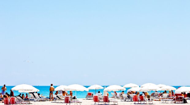 People enjoy a sunny day under beach umbrellas on the sandy shore, 4K Desktop Wallpaper