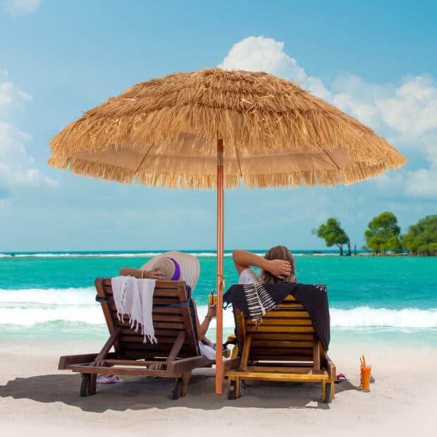 Two people enjoy the ocean view under a beach umbrella on the sandy shore, HD Desktop Wallpaper