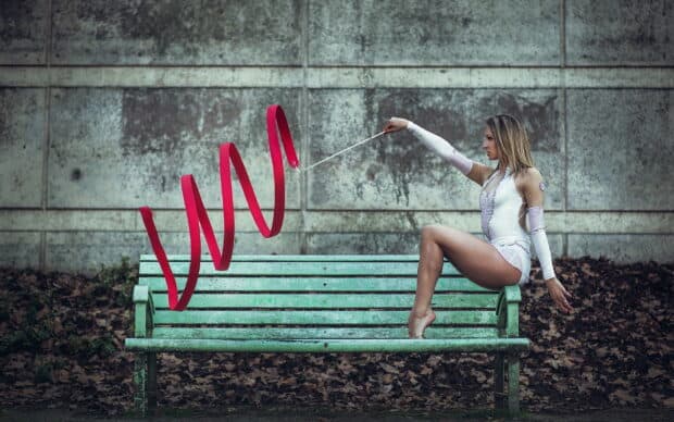 A rhythmic gymnast performs with a red ribbon while sitting on a green bench, HD Desktop Wallpaper