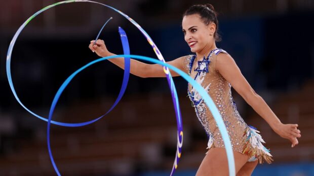A rhythmic gymnastics athlete is smiling while performing a ribbon routine in a competition, 2K Desktop Wallpaper