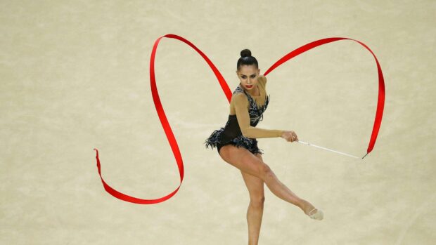 A rhythmic gymnastics athlete moves gracefully with a red ribbon during a competition, HD Desktop Wallpaper
