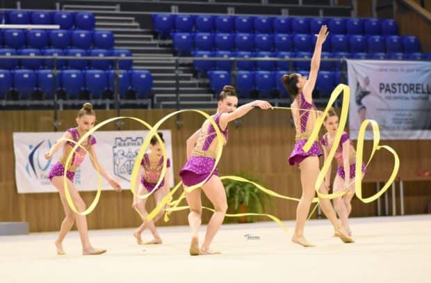 A group of rhythmic gymnasts is performing a coordinated ribbon routine in a sports hall, HD Desktop Wallpaper