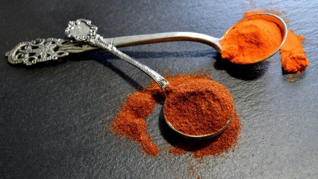Two spoons hold red seasoning powder on a dark surface with some spilled around them, HD Desktop Wallpaper