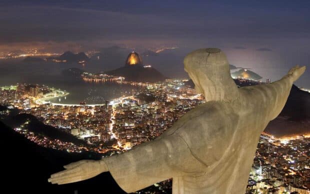 The Rio de Janeiro cityscape is illuminated with night lights under a cloudy sky, 2K Desktop Wallpaper
