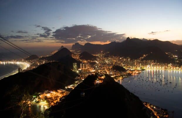 The vibrant Rio De Janeiro Wallpapers city skyline glows as night falls over the mountains and coastline, 2K Desktop Wallpaper