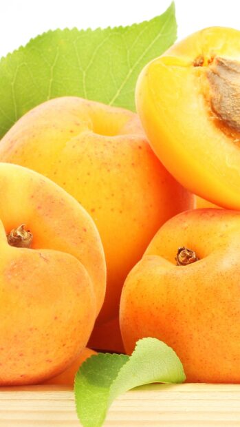 A close up of ripe apricot fruits with green leaves arranged on wooden surface, 4K Mobile Wallpaper