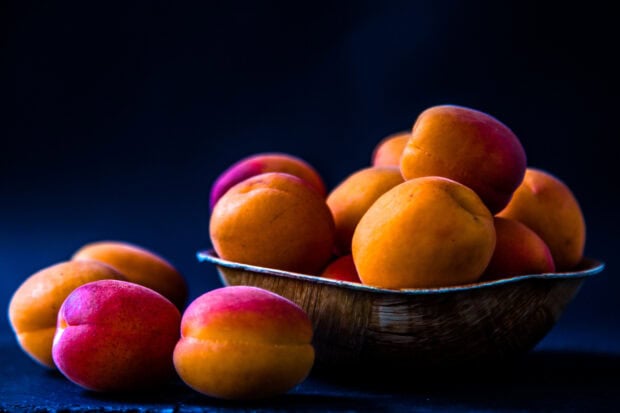 A bowl filled with ripe apricots resting on a dark surface, HD Desktop Wallpaper
