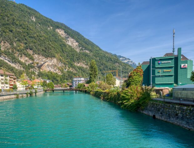 The River Aare flows through a town surrounded by green mountains under a clear blue sky, HD Desktop Wallpaper