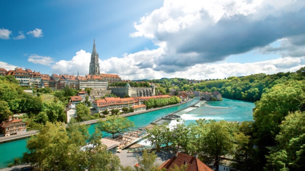The River Aare in Switzerland flows beside historic buildings and lush greenery under a partly cloudy sky, HD Desktop Wallpaper