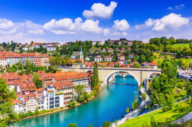 A scenic view of River Aare Switzerland with buildings and green hills under blue sky, HD Desktop Wallpaper