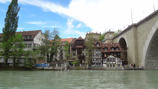 The River Aare flows past historic buildings and a stone bridge in Switzerland, HD Desktop Wallpaper