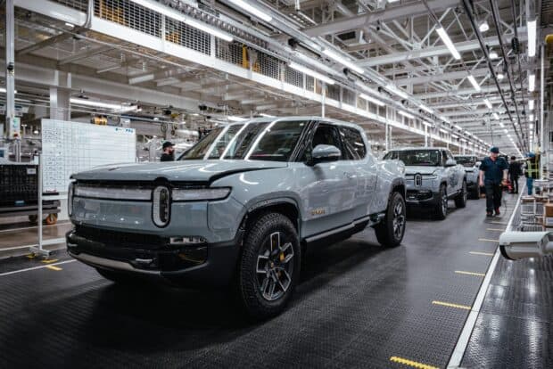 Rivian automotive electric pickup truck lined up in a factory with workers nearby, HD Desktop Wallpaper