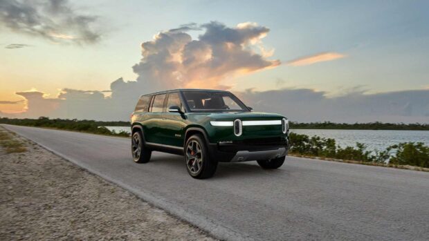 A Rivian electric SUV is driving along a road near water under a cloudy sky during sunset, HD Desktop Wallpaper